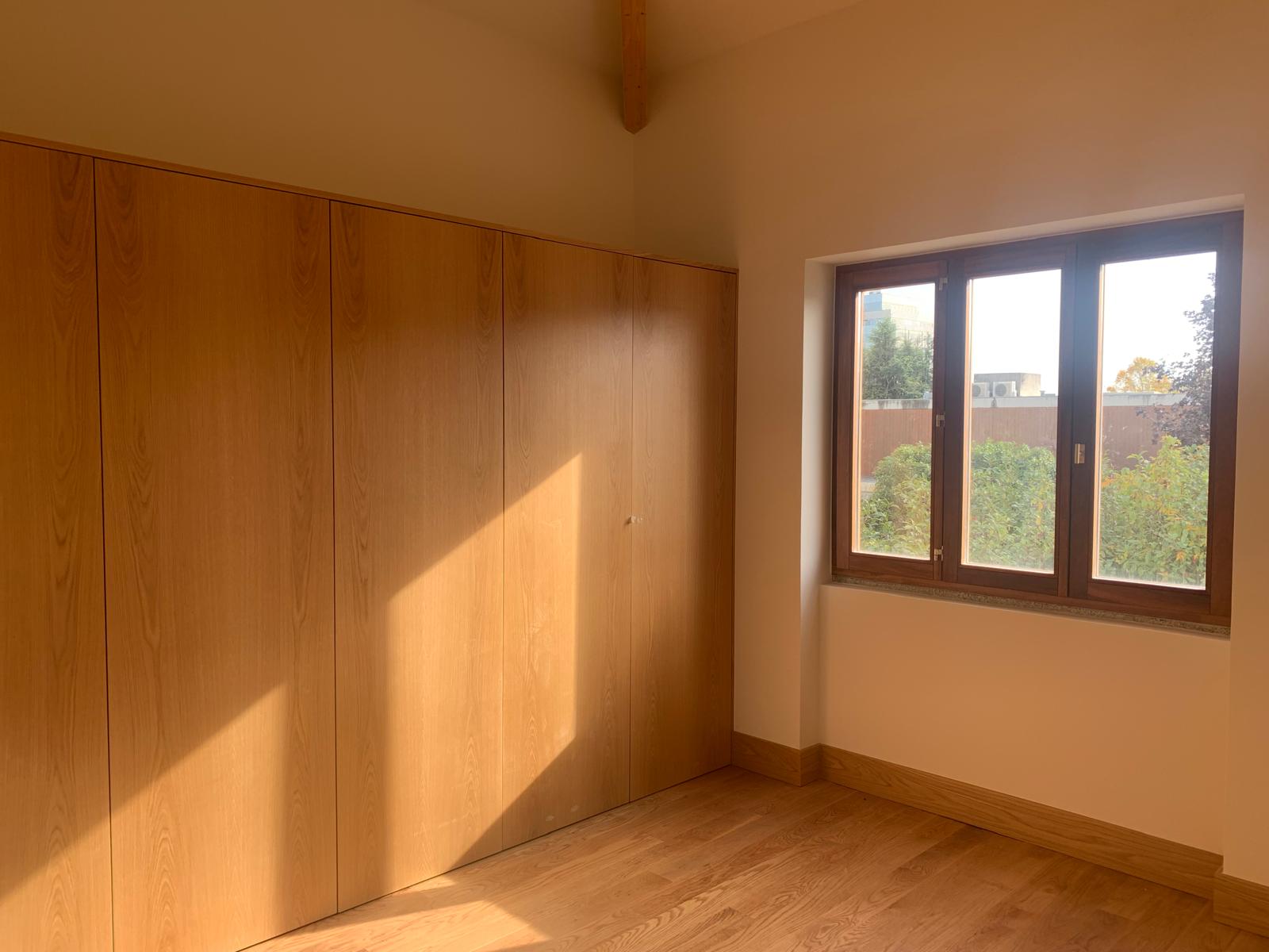 Bedroom with full-wall oak wardrobes, timber window frame and oak floor in warm light