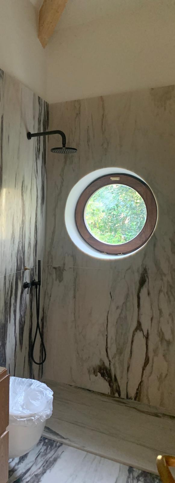 Shower lined in veined Portuguese marble with a round timber-framed window